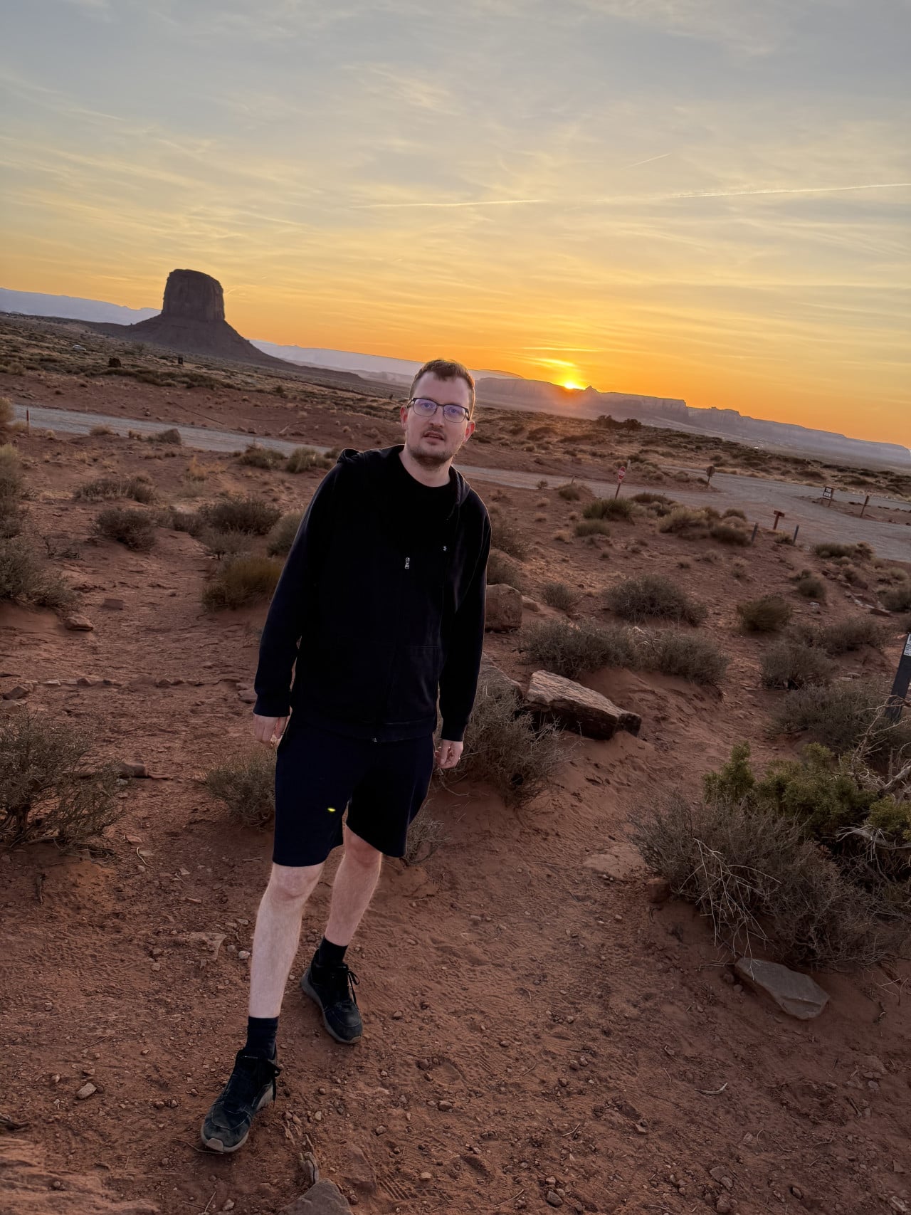 Muž v černé mikině na poušti, v pozadí západ slunce a stolová hora