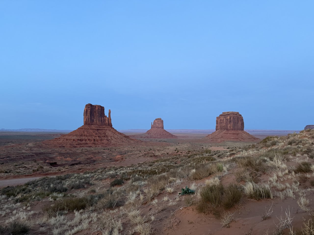 Monument Valley za soumraku, tři pískovcové butty na obzoru, step vpředu
