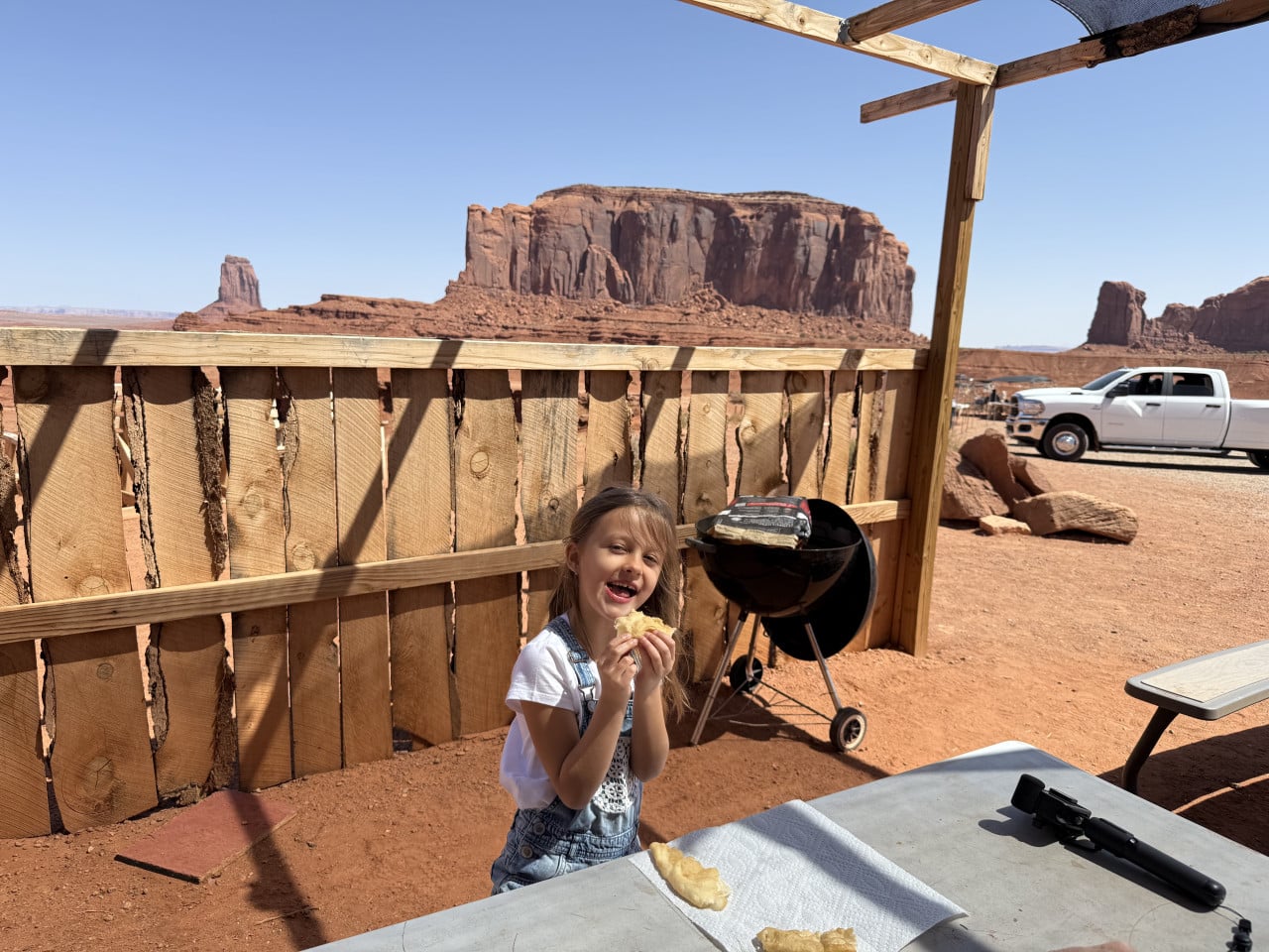 Dítě jí na terase u grilu, v pozadí monumenty Monument Valley a pick-up.