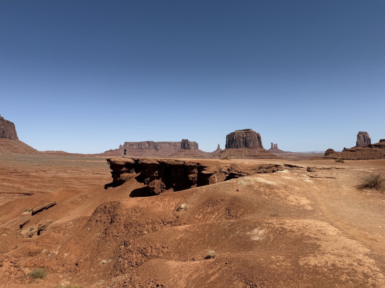 Postava na skalním převisu, v dálce stolové hory Monument Valley