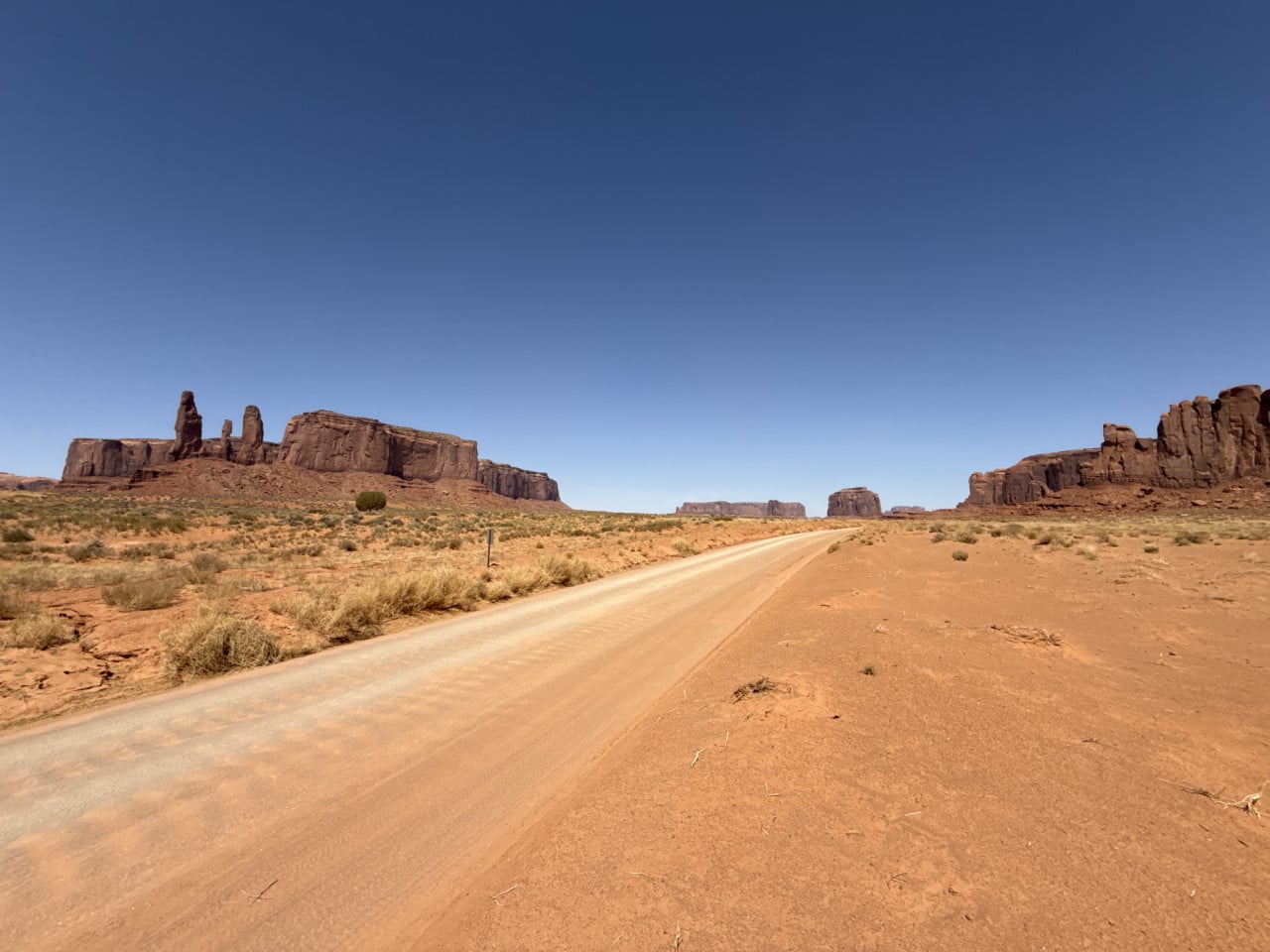 Prašná cesta v Monument Valley, červená poušť a skalní monumenty pod modrou oblohou