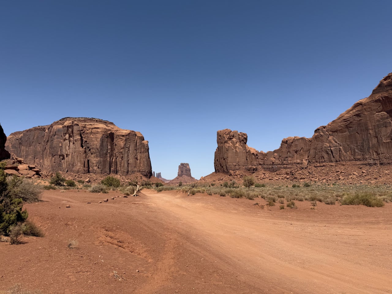 Prašná cesta mezi pískovcovými stolovými horami v Monument Valley pod modrou oblohou