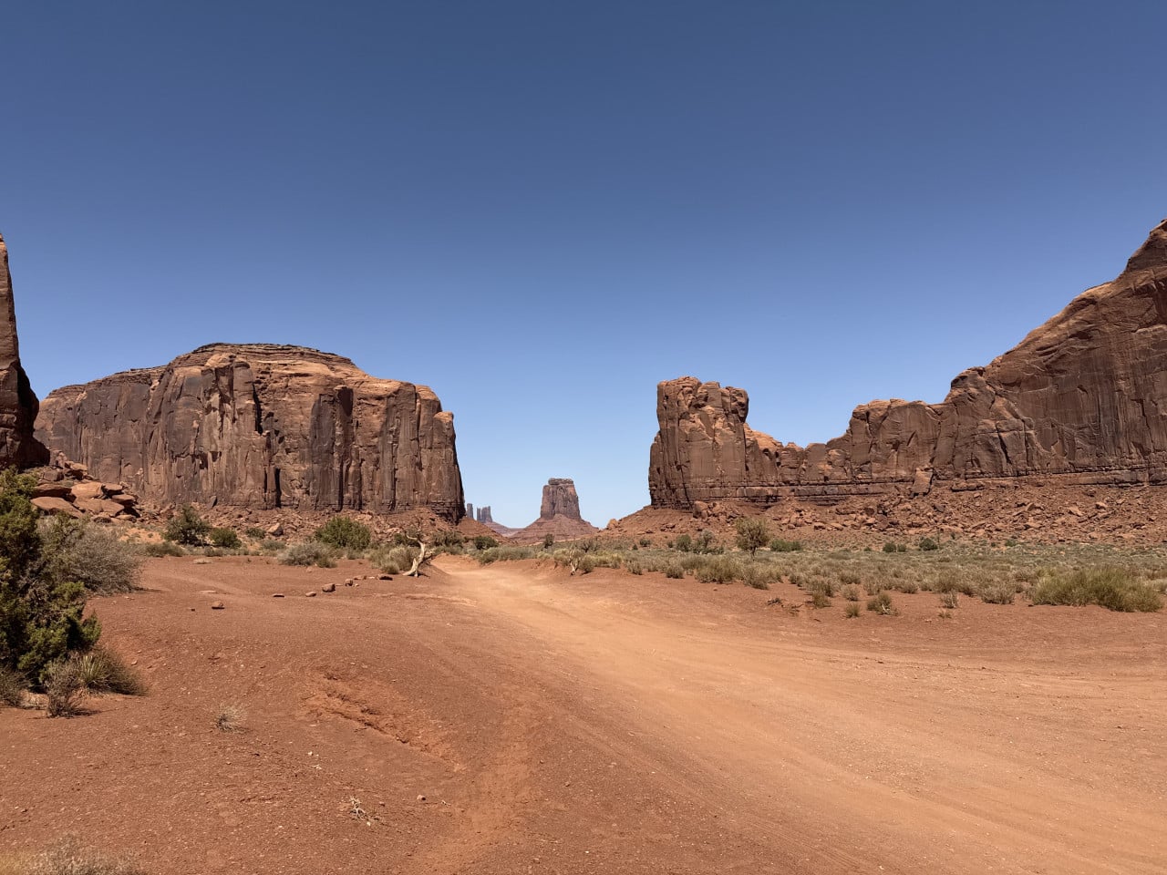 Prašná cesta v Monument Valley mezi červenými skalními monumenty pod modrou oblohou
