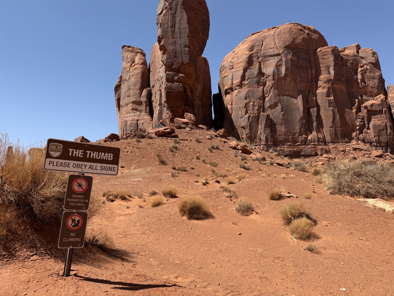 Skalní věže Monument Valley; cedule THE THUMB, DRONES PROHIBITED IN THIS AREA, NO CLIMBING