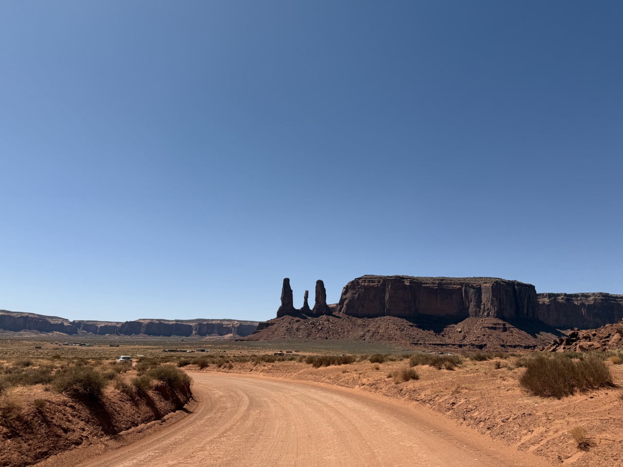 Prašná cesta v poušti, v dálce monumenty a stolové hory Monument Valley