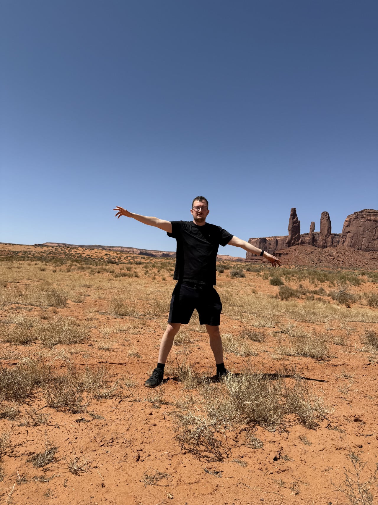 Muž s rozpaženýma rukama na poušti, v pozadí skalní věže Monument Valley
