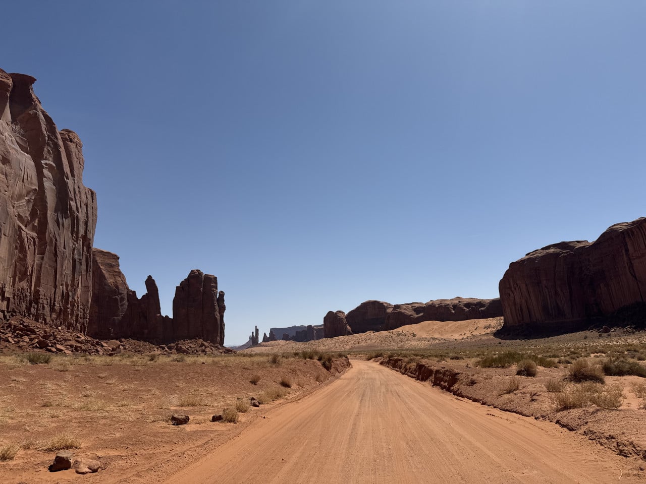 Prašná cesta v Monument Valley mezi skalními monumenty pod jasnou oblohou