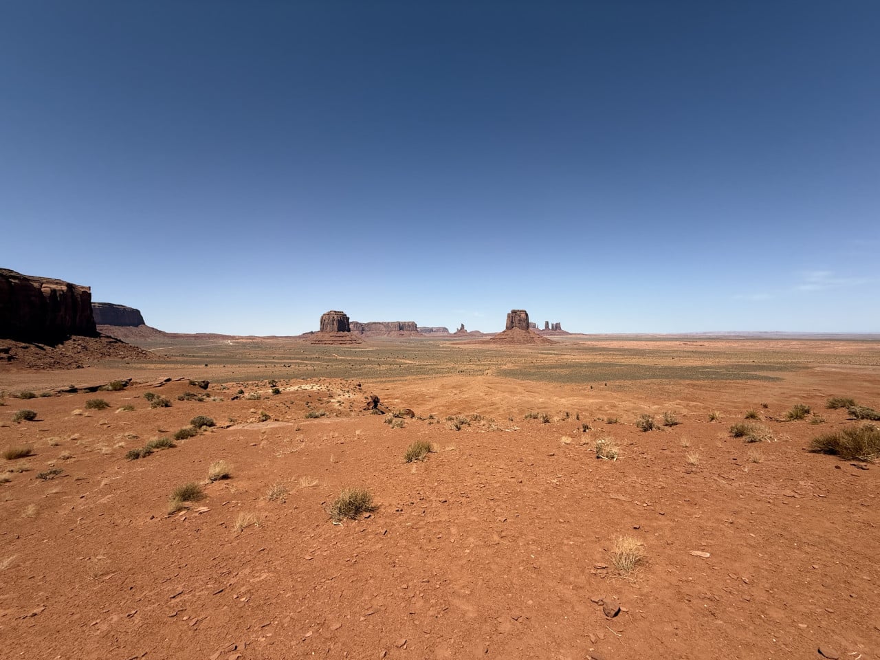 Široká poušť Monument Valley s červenou půdou, keři a vzdálenými skalními věžemi