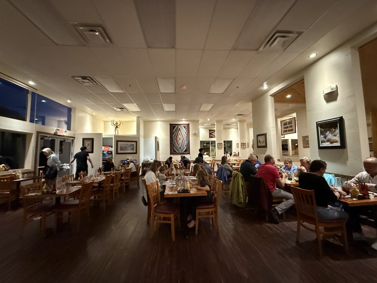 Jídelna hotelové restaurace s hosty u stolů, cedule AHÉ HÉÉ THANK YOU COME AGAIN