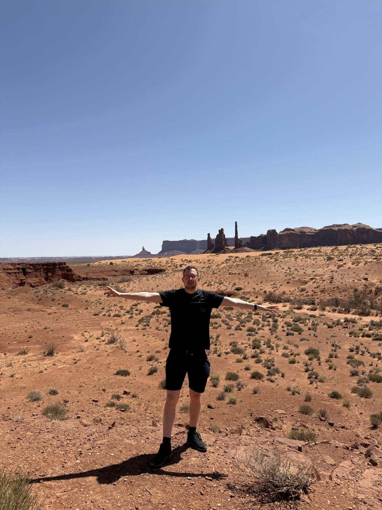 Muž s rozpaženýma rukama na poušti, v pozadí monumenty Monument Valley.