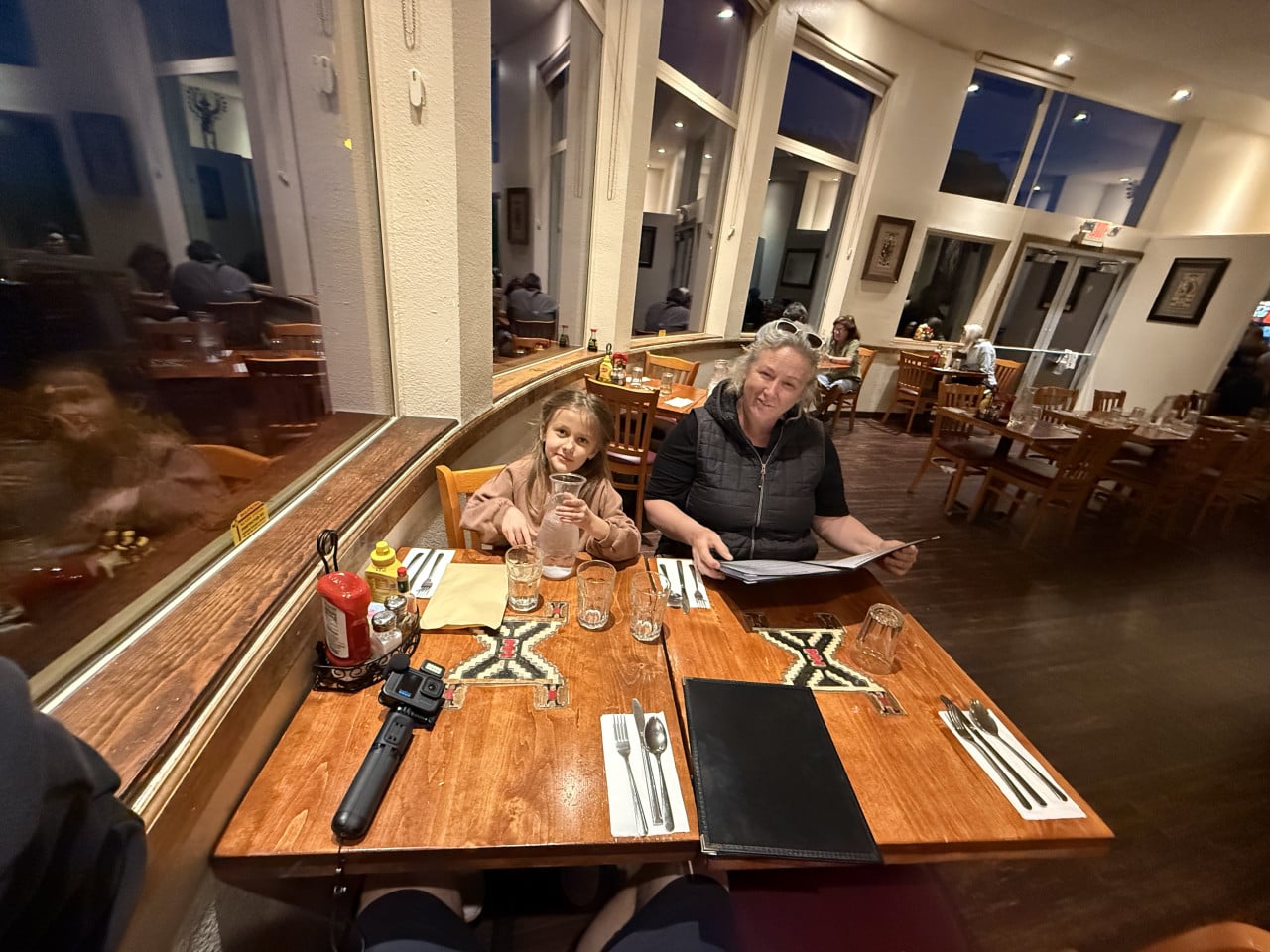 Žena a dítě u stolu v restauraci, před nimi menu, voda a kamera