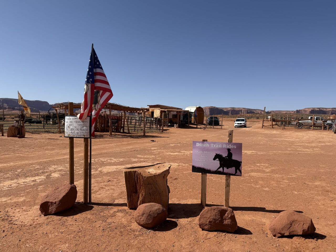 Americká vlajka v poušti, cedule Dinéh Trail Rides, ohrady a auta