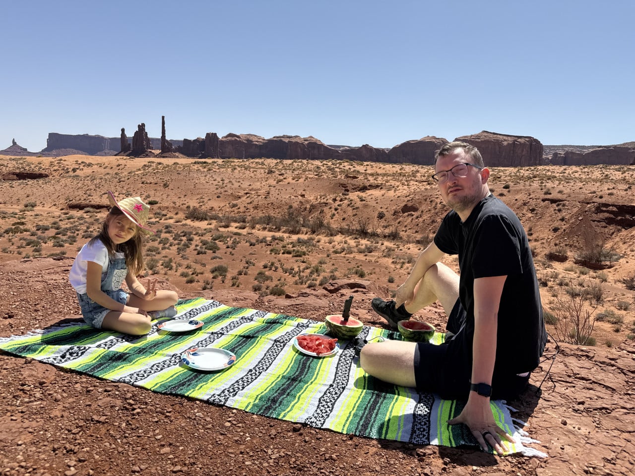 Muž a dívka na dece s melounem, v pozadí skály Monument Valley