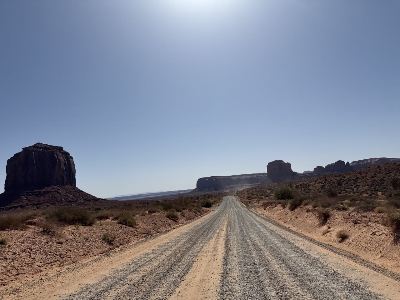 Štěrková cesta v Monument Valley, pouštní krajina a skalní monumenty v dálce