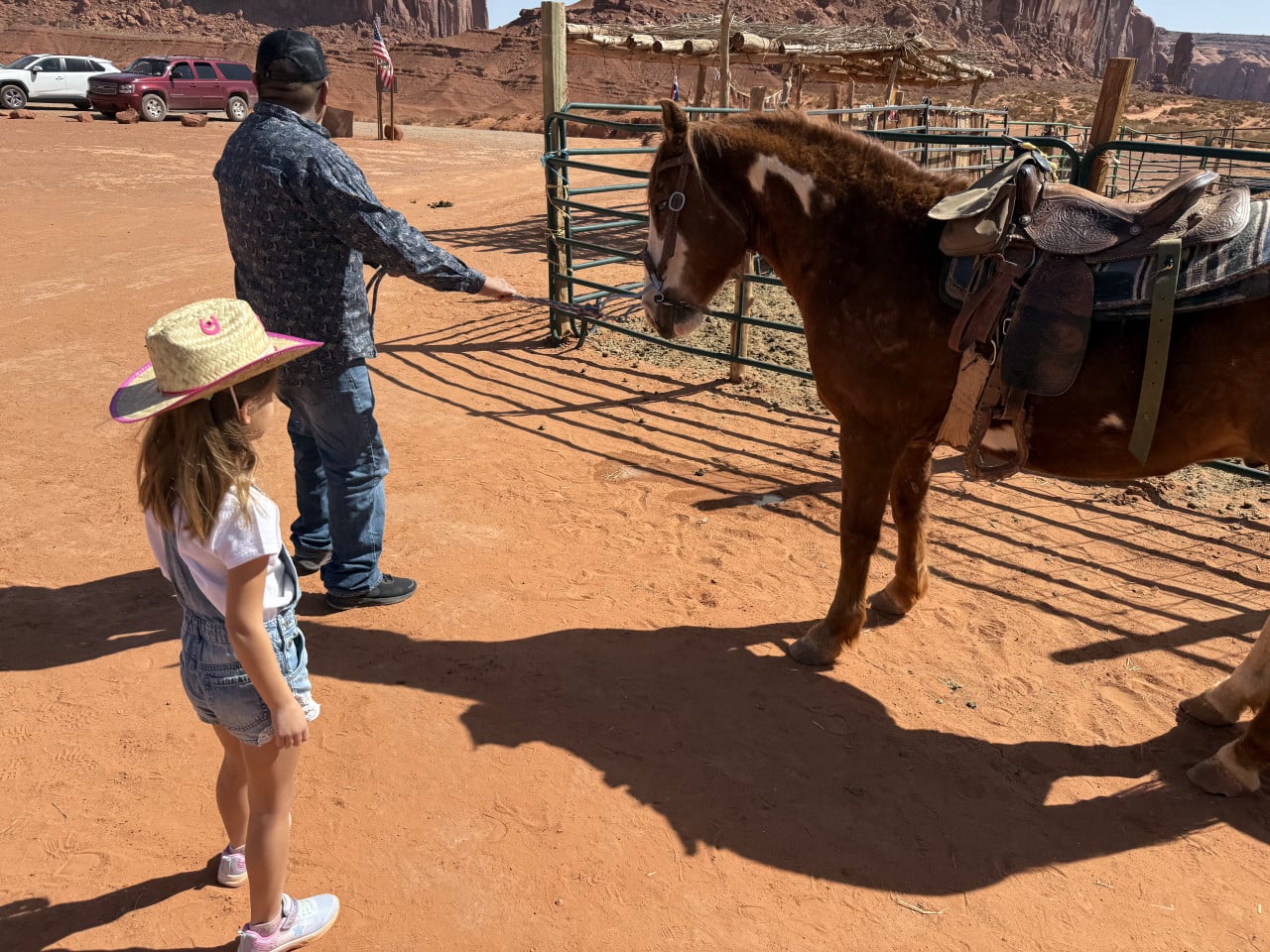 Holčička a muž u ohrady se sedlaným koněm, v pozadí skalní věže
