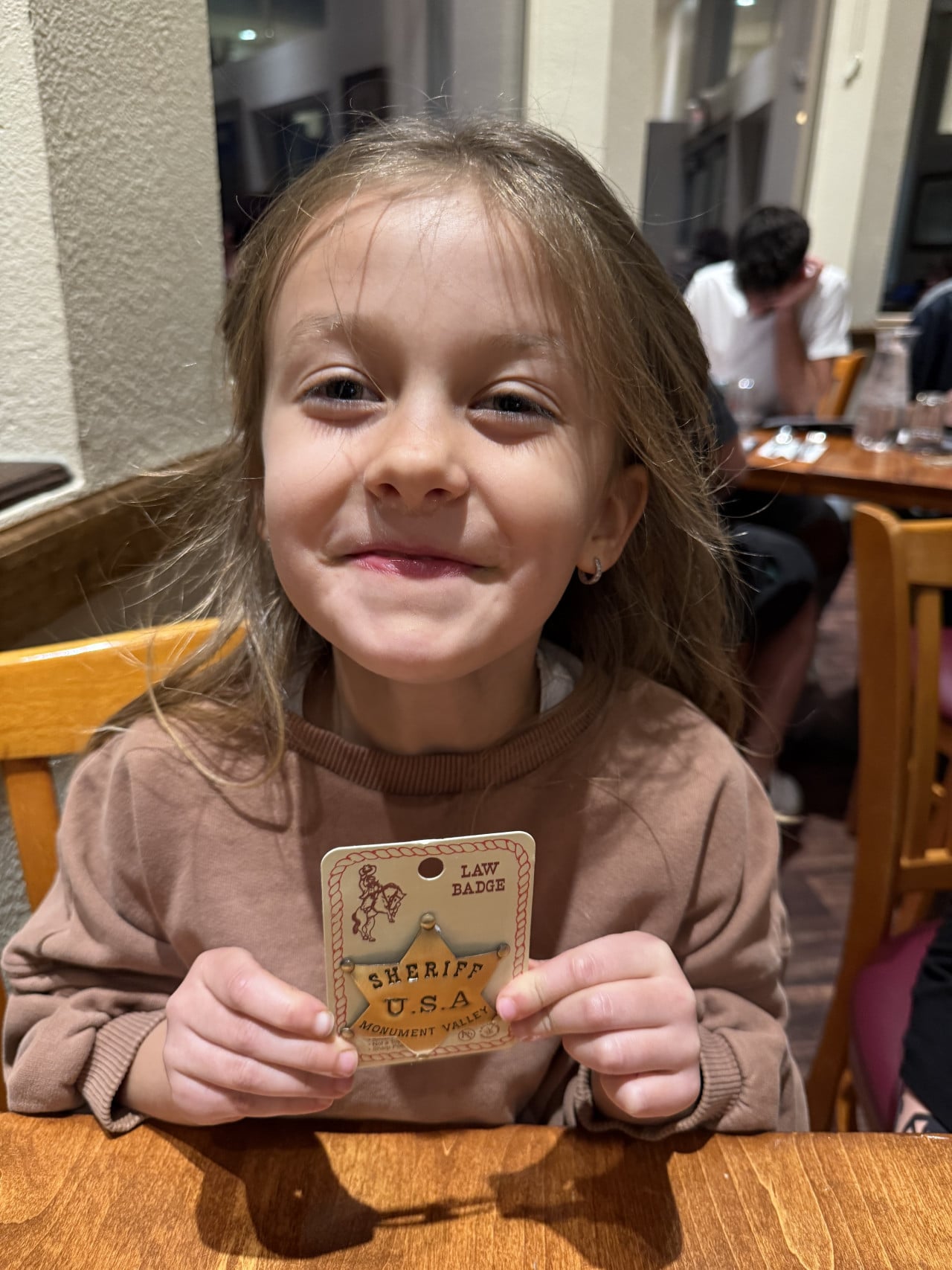 Usměvavá holčička v restauraci drží odznak LAW BADGE SHERIFF U.S.A MONUMENT VALLEY.
