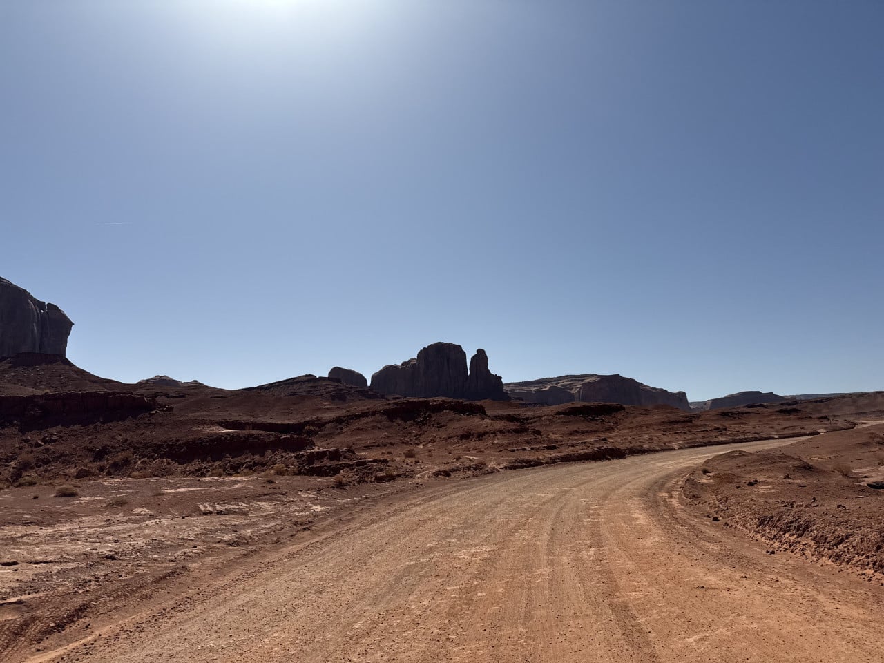 Prašná cesta v Monument Valley, v dálce skalní monumenty pod modrou oblohou