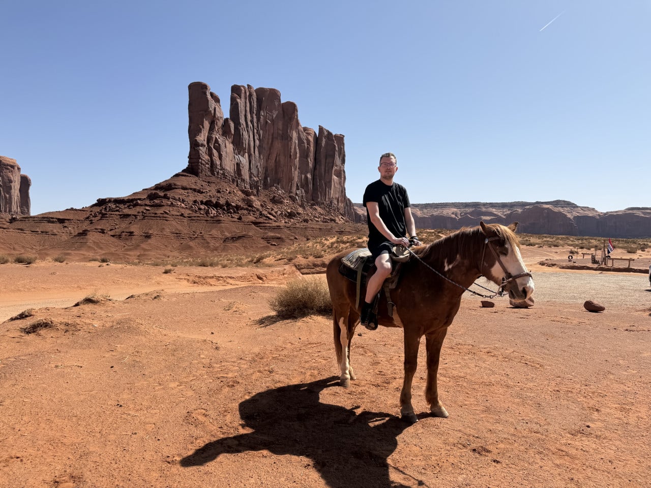Muž sedí na koni v Monument Valley, za ním červené skalní věže