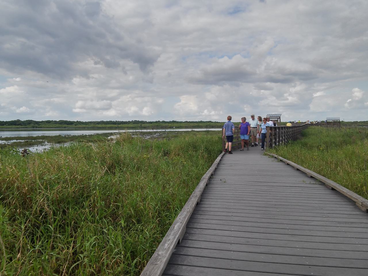 Dřevěná lávka přes mokřad s turisty a zamračenou oblohou