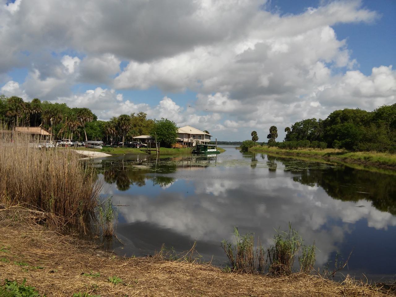 Klidná řeka v Myakka River State Park s odrazem mraků a lodí u břehu