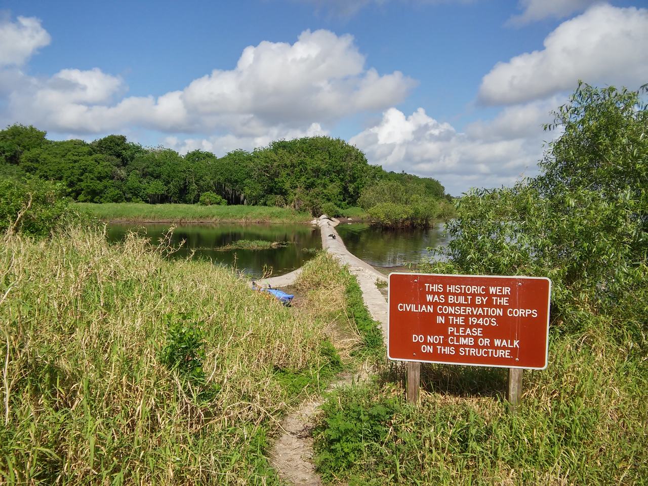 Pohled na mokřad s historickým jezem a výstražnou cedulí v Myakka River State Parku