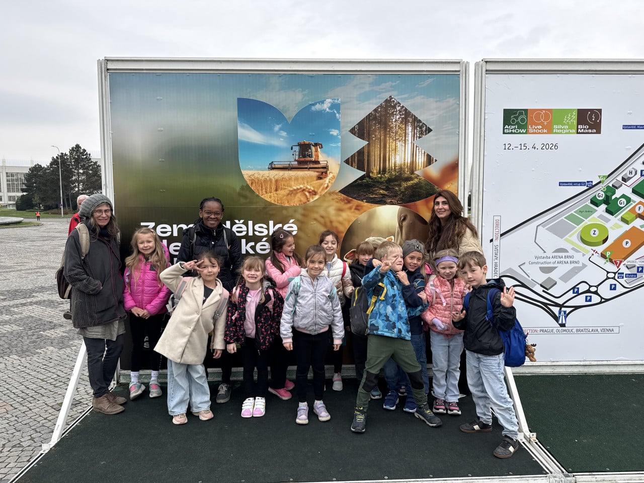 Skupina školáků a učitelek pózuje před billboardem Národní výstavy hospodářských zvířat v Brně.