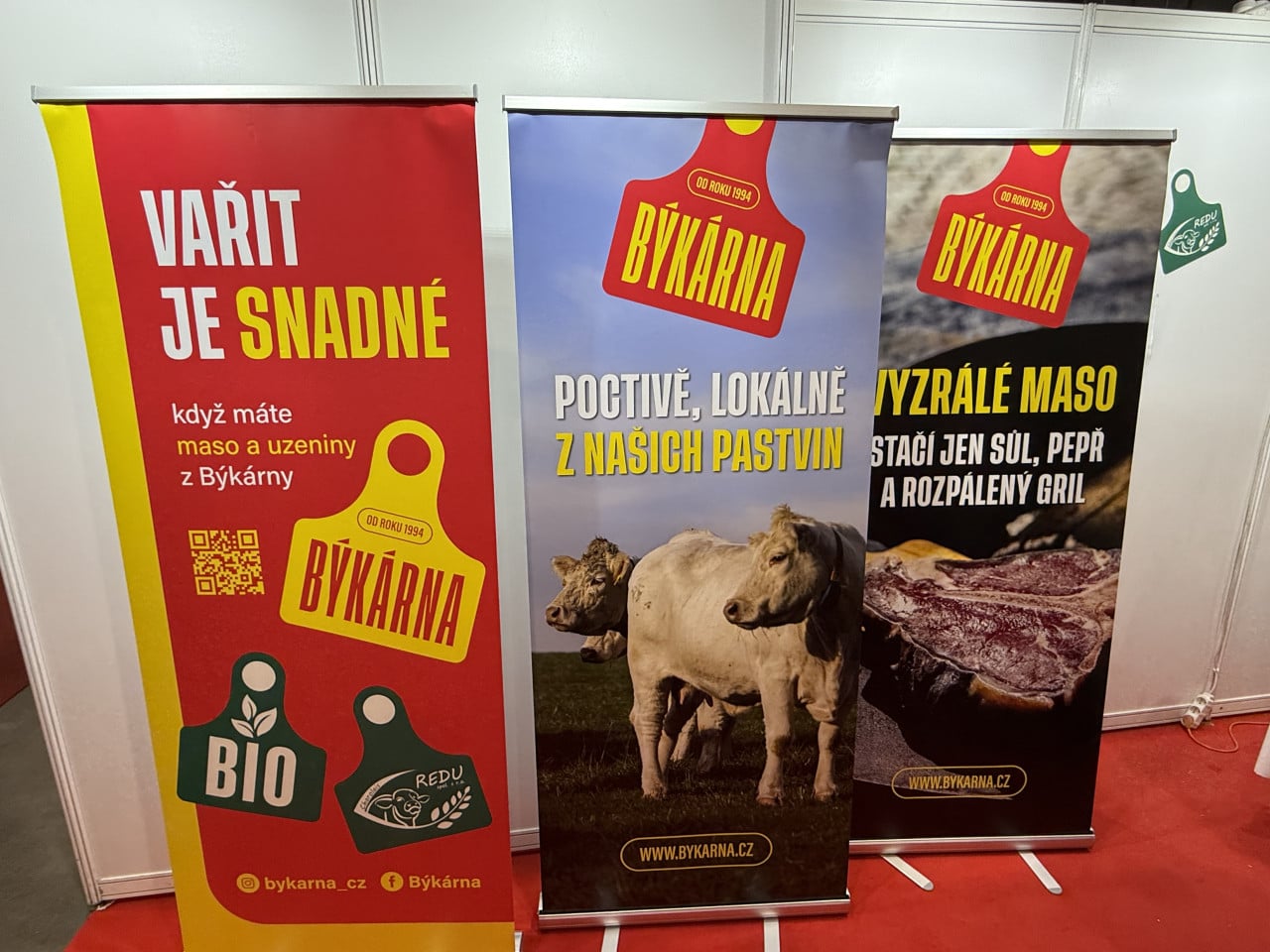 Reklamní bannery Býkárna s nápisy o masu, pastvinách a hovězím mase.