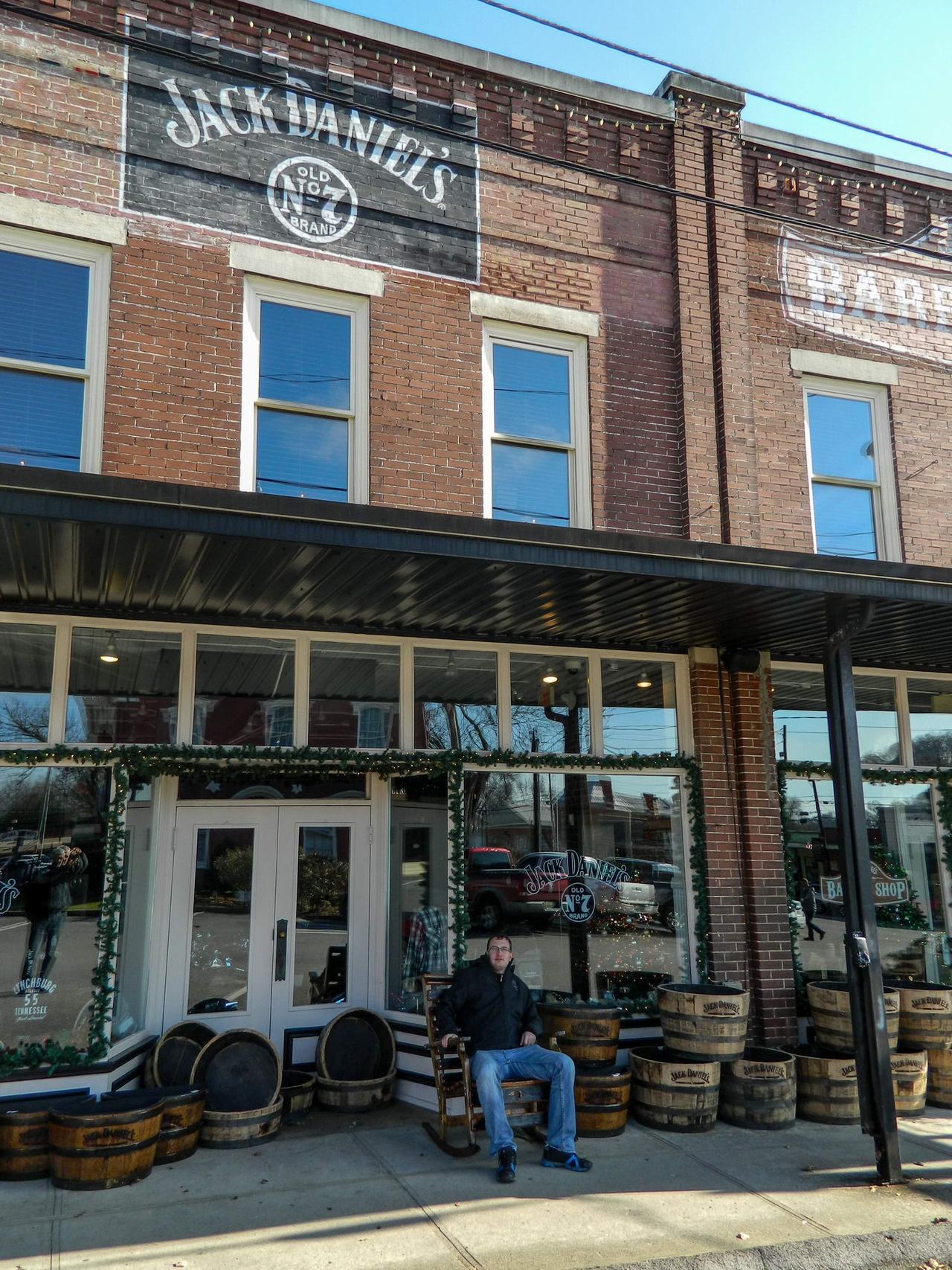 Cihlový dům s nápisem JACK DANIEL'S Old No.7, sudy, muž na židli