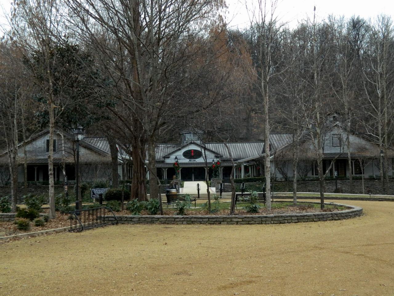 Vstupní budova destilerie Jack Daniel’s mezi stromy, cedule WELCOME nad vchodem.