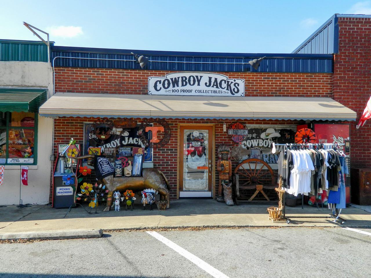 Fasáda obchodu COWBOY JACK'S 100 PROOF COLLECTIBLES, před ním stojany s oblečením