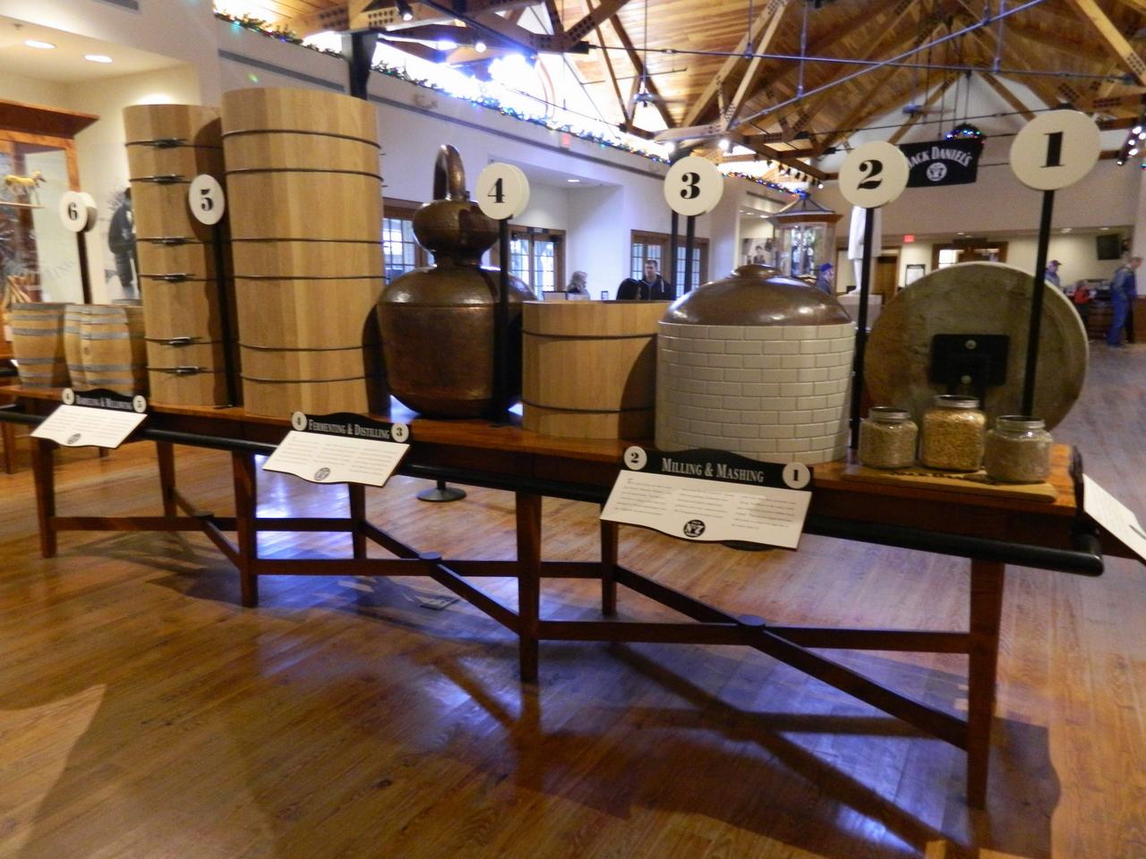 Expozice v destilerii: sudy, měděný kotel a cedule Milling & Mashing, Fermenting & Distilling