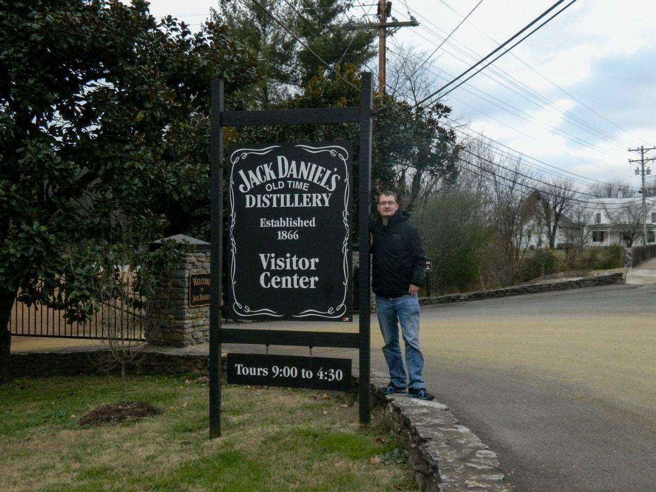 Muž u cedule Jack Daniel’s Old Time Distillery, Visitor Center, Tours 9:00–4:30.