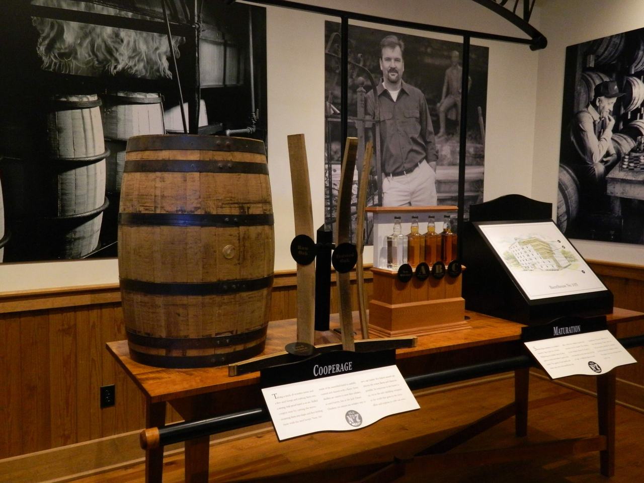 Expozice destilerie: dřevěný sud, nástroje, láhve a cedule COOPERAGE, MATURATION.