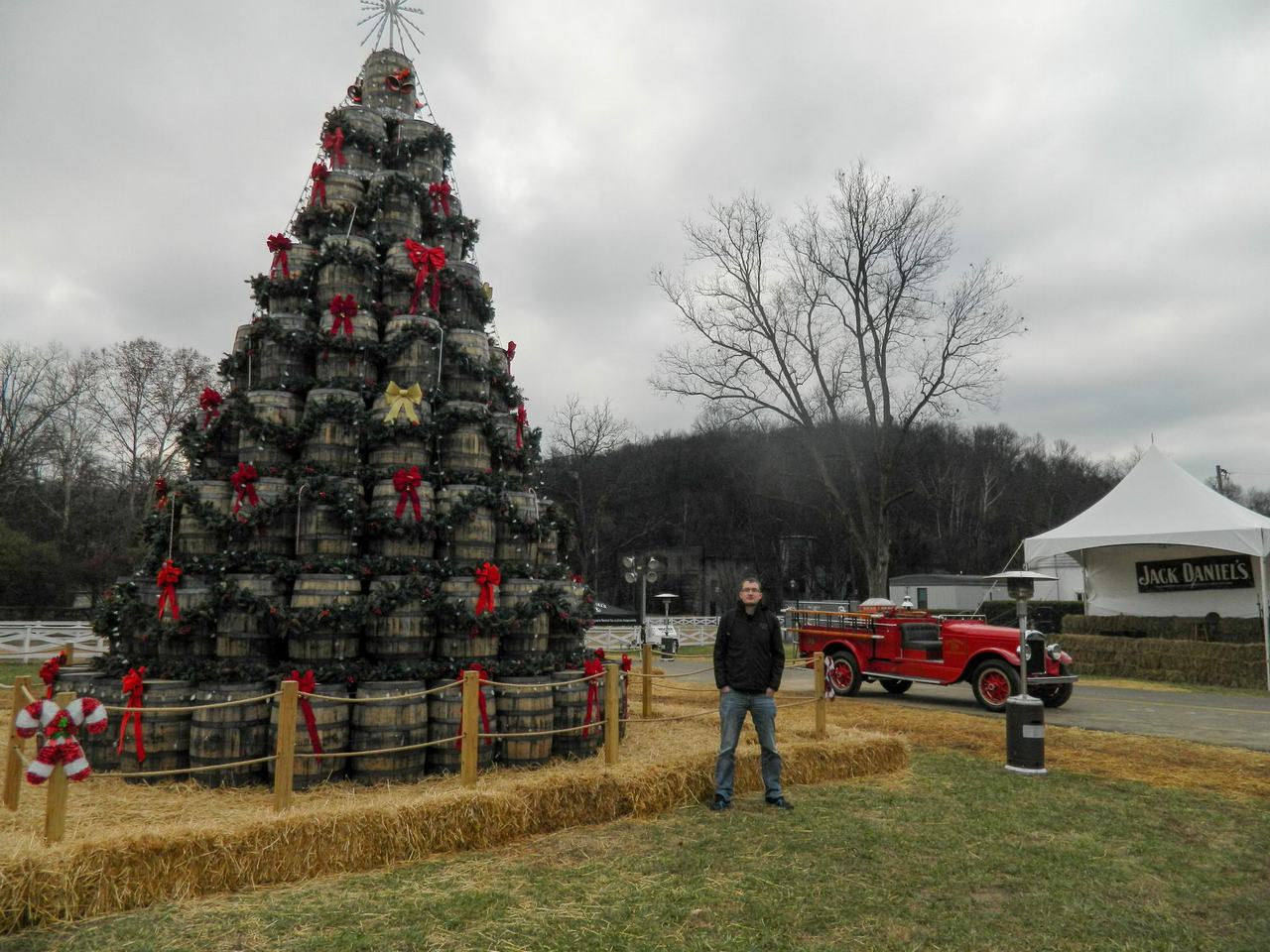 Muž před vánočním stromem z whisky sudů, vedle červený veterán, stan Jack Daniel’s.