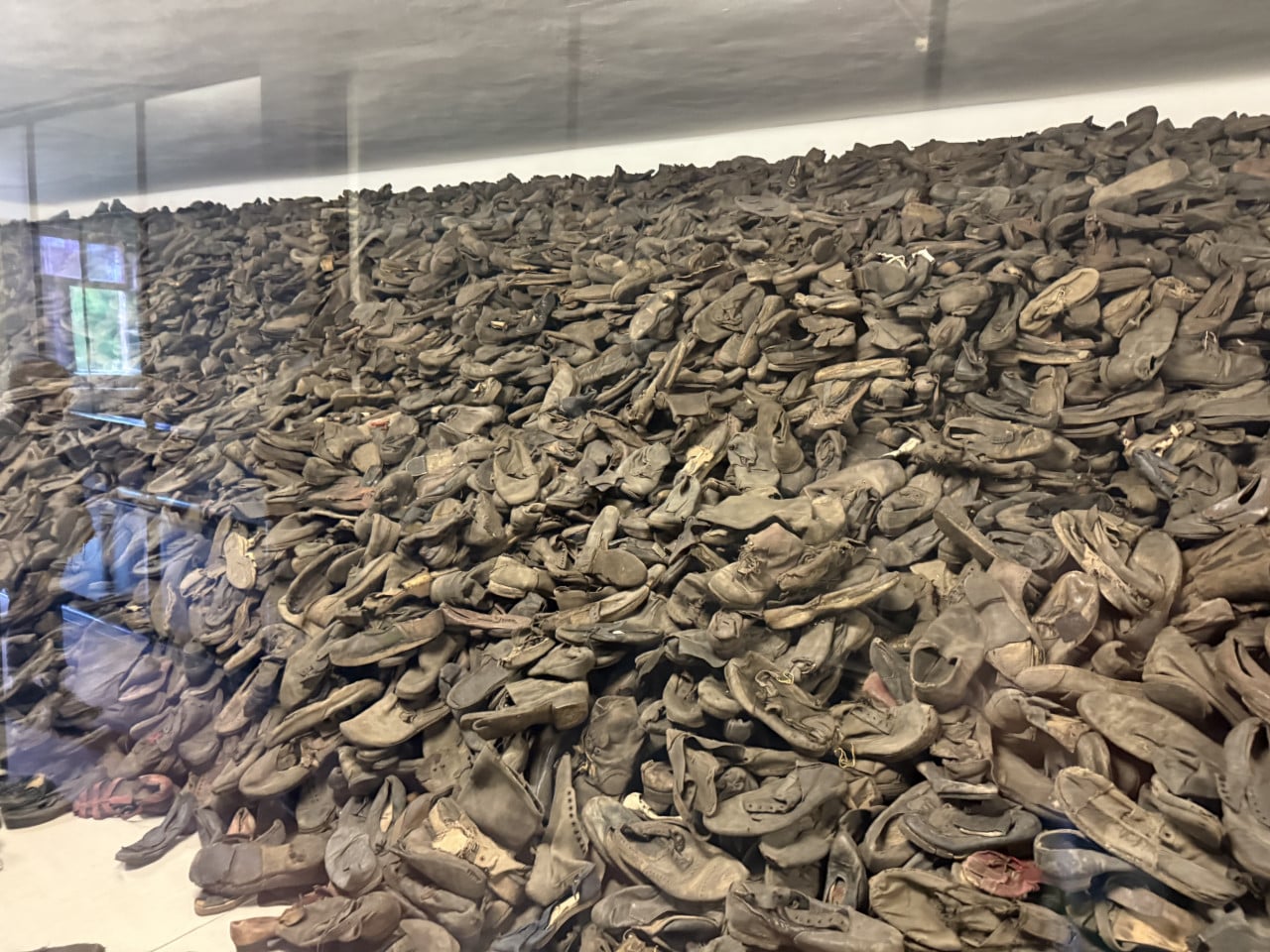 Hromada opotřebovaných bot za sklem v muzeu Auschwitz-Birkenau