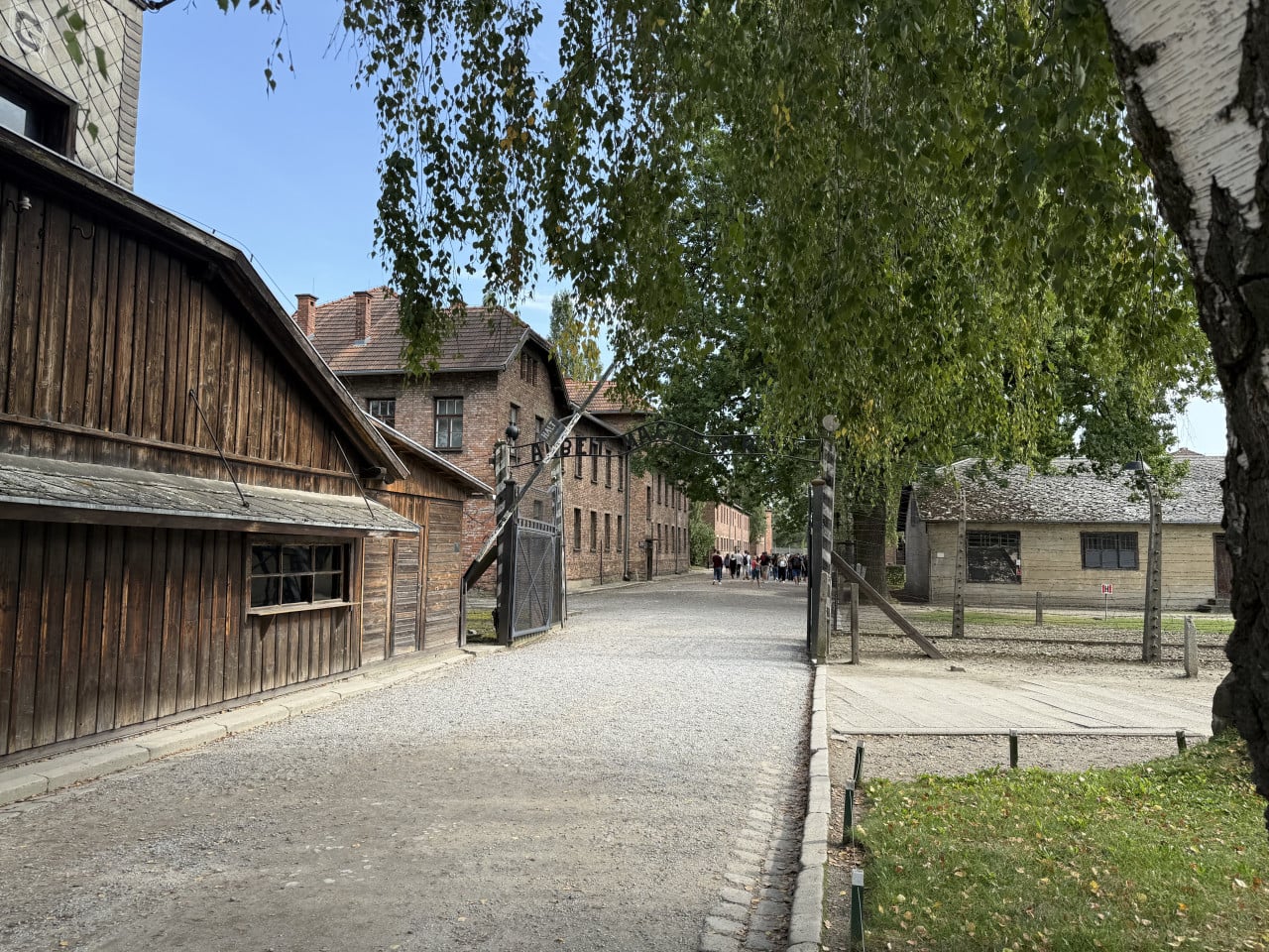Vstupní brána Auschwitz-Birkenau s nápisem Arbeit Macht Frei a návštěvníky na cestě.