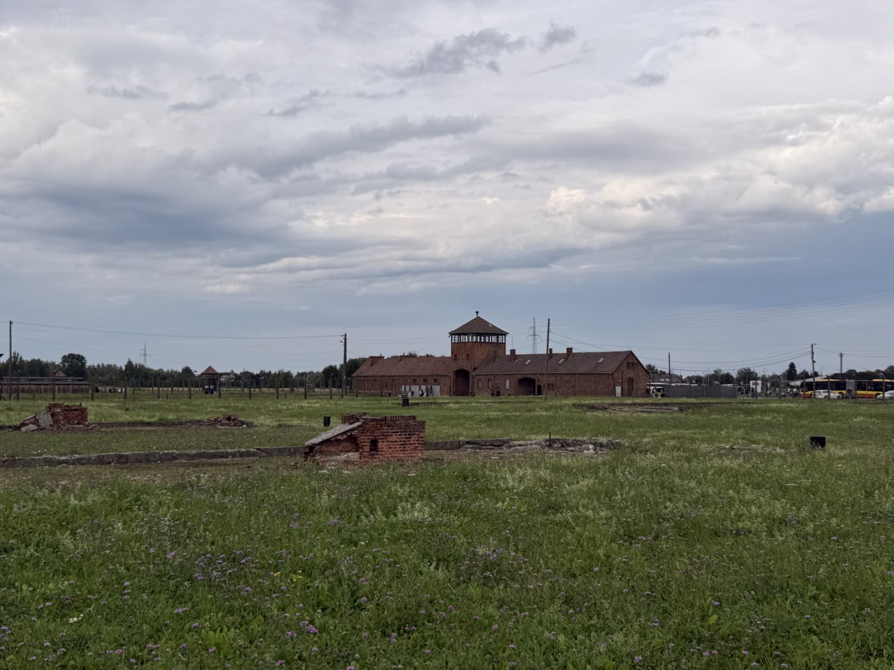 Areál Auschwitz-Birkenau s cihlovou budovou, travnatým polem a zamračenou oblohou