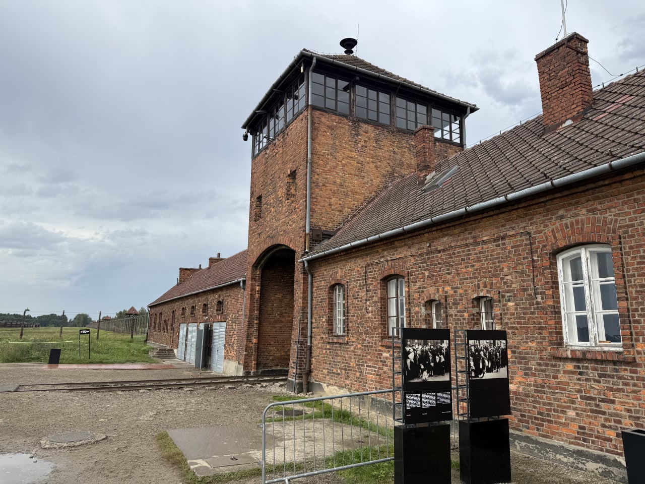 Cihlová budova strážní věže Auschwitz s informačními panely a kolejemi před ní