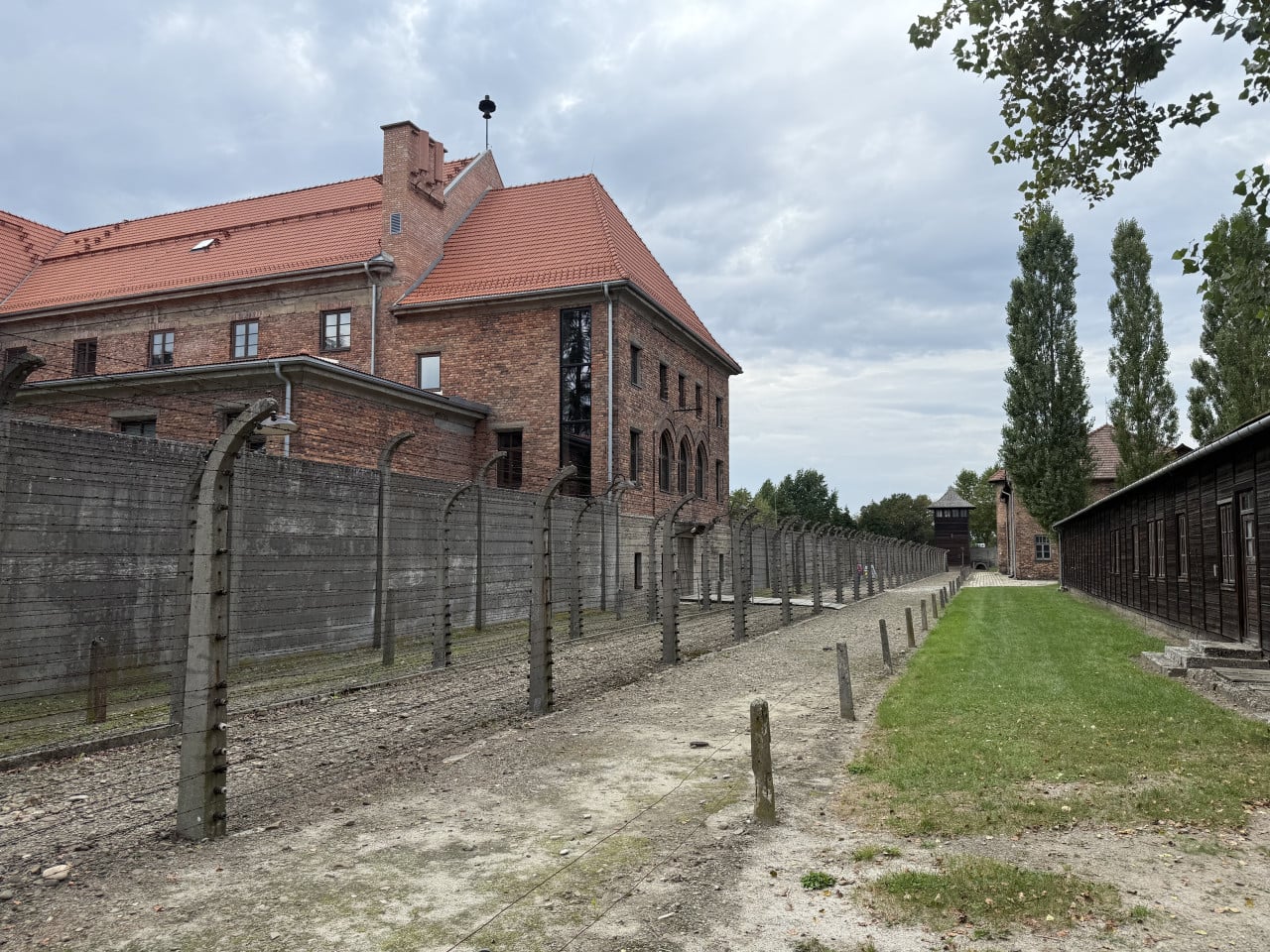 Pohled na cihlové budovy Auschwitz za ostnatým drátem a strážní věží