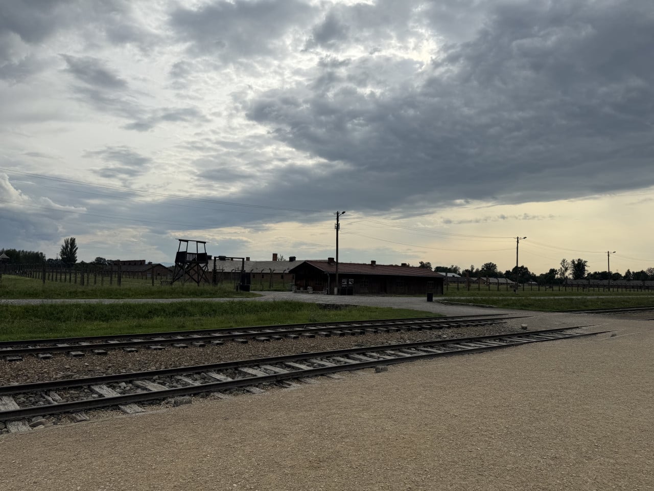 Pohled na koleje, strážní věž a baráky v Birkenau pod zamračenou oblohou
