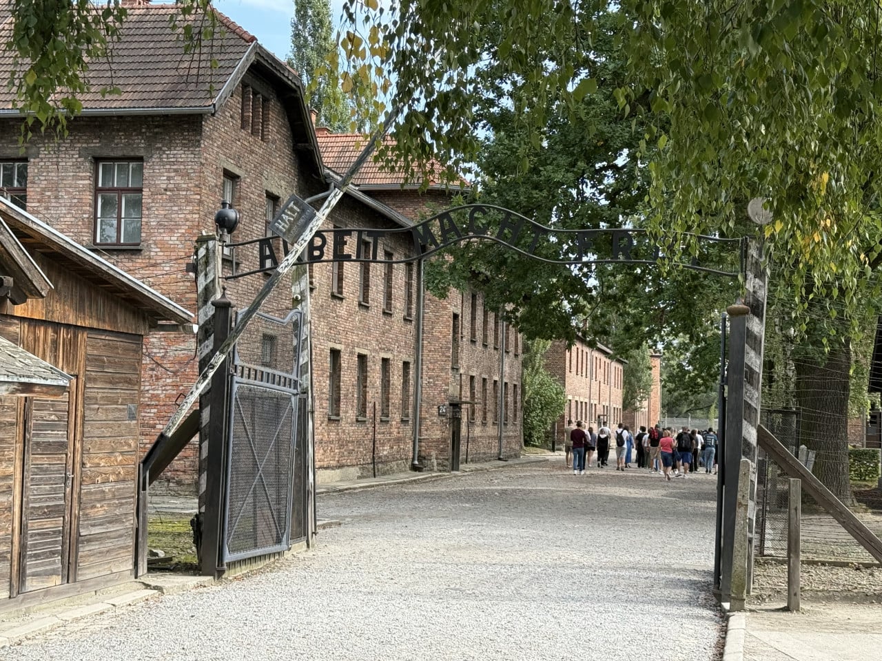 Vstupní brána Auschwitz s nápisem Arbeit Macht Frei a skupinou návštěvníků.