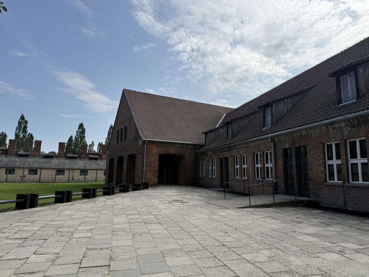 Nádvoří Auschwitz-Birkenau s cihlovými budovami a modrou oblohou s mraky