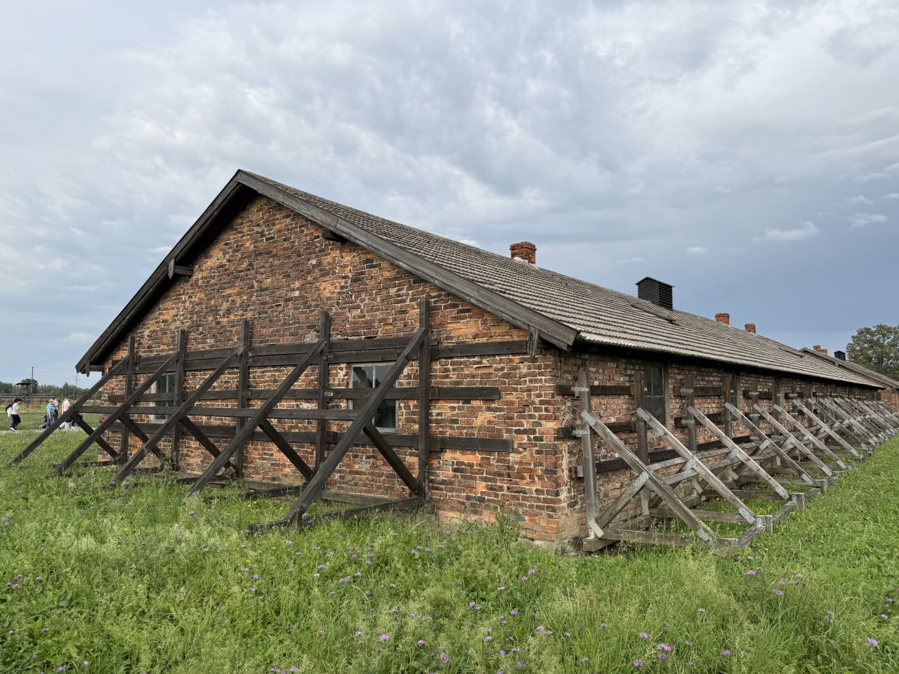 Cihlový barák v Auschwitz s dřevěnými výztuhami a travnatým polem под zataženou oblohou