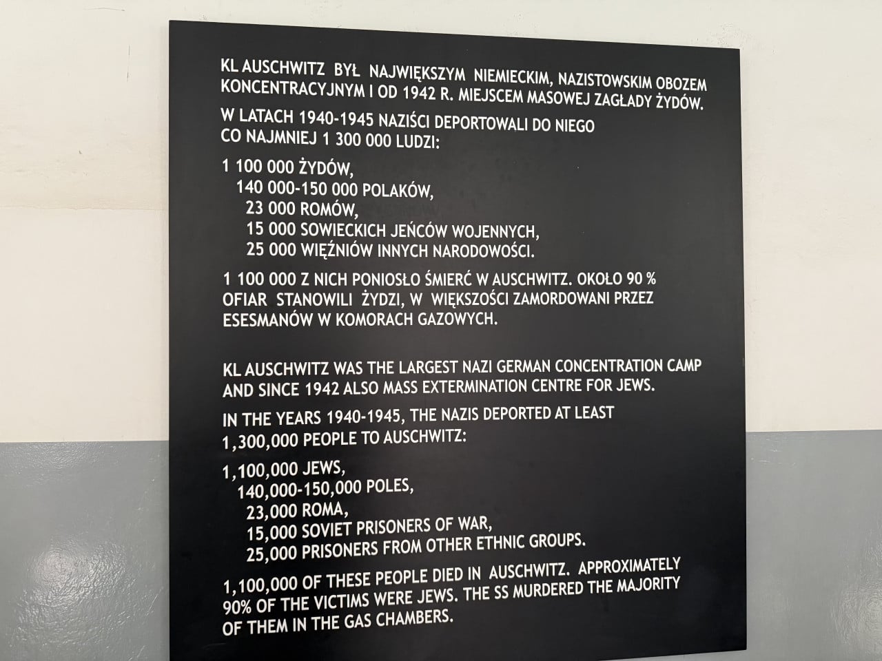 Černá informační tabule s textem o historii a obětech Auschwitz v polštině a angličtině