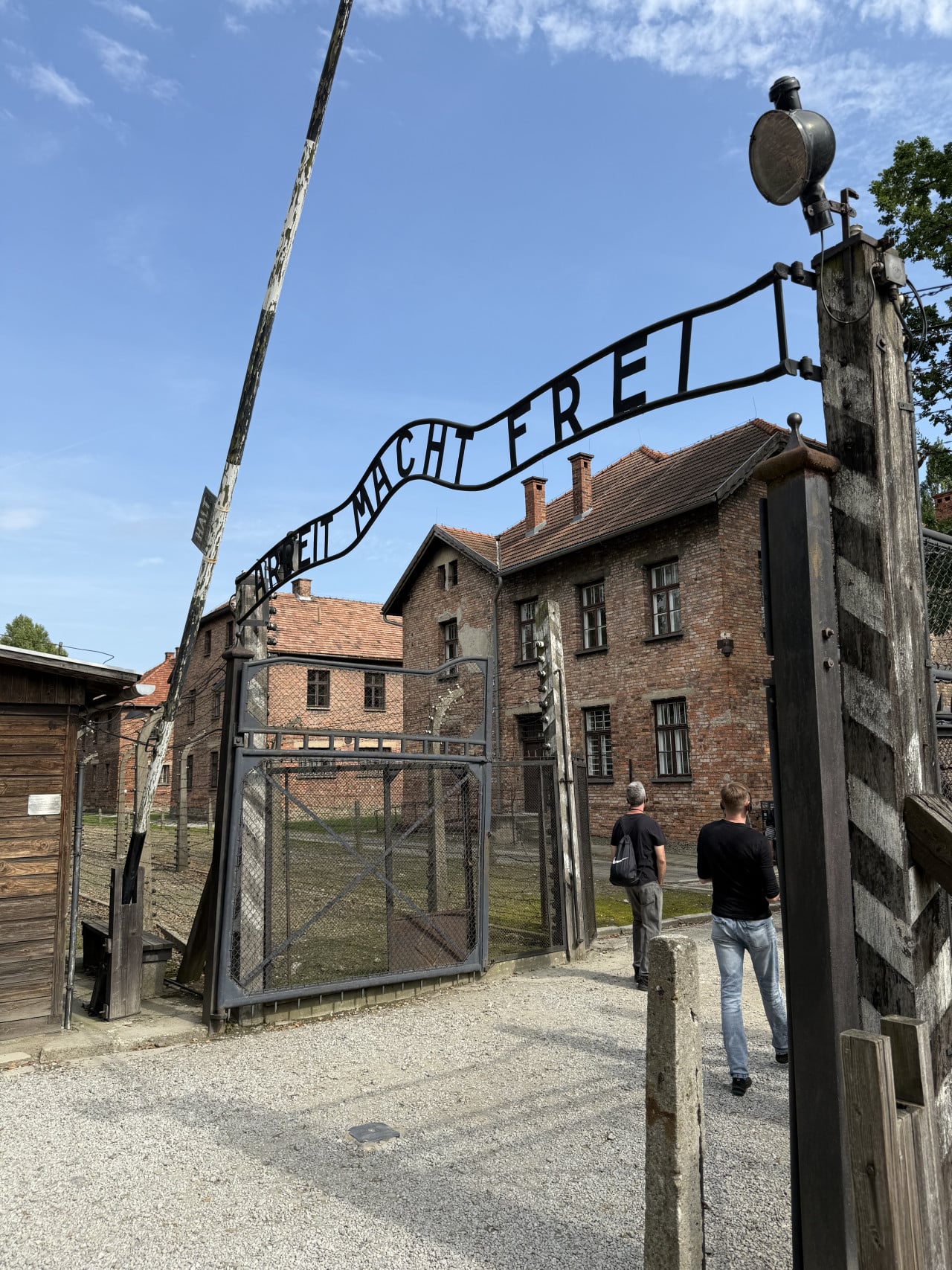 Vstupní brána Auschwitz s nápisem Arbeit Macht Frei a dvěma návštěvníky