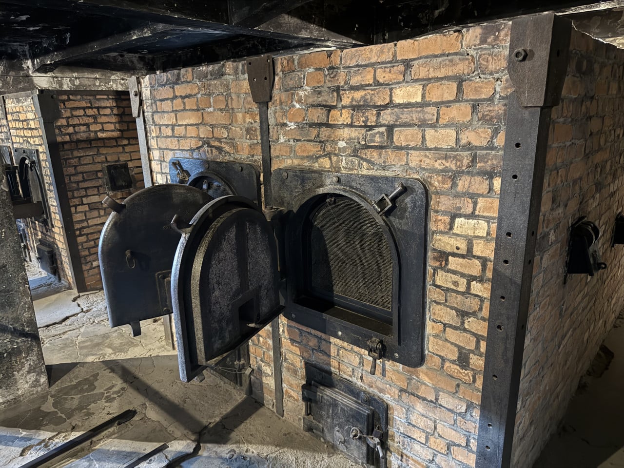 Otevřená cihlová pec s kovovými dvířky a roštem v muzeu Auschwitz-Birkenau