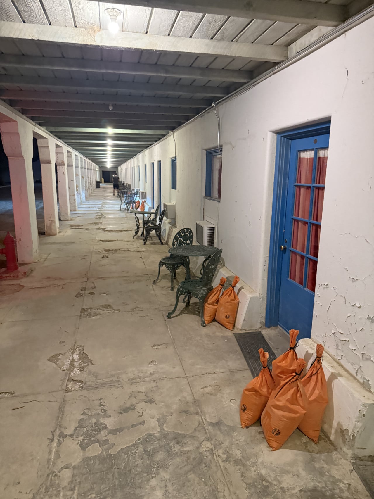 Chodba hotelu s modrými dveřmi, židlemi a oranžovými pytli u stěny