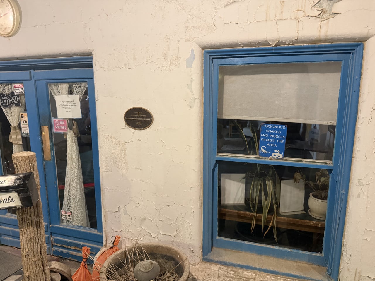 Modré dveře a okna starého hotelu s nápisy Closed a Poisonous snakes and insects inhabit the area.
