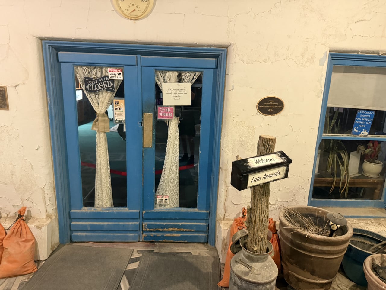 Modré dveře Amargosa Opera House s nápisy Closed a Late Arrivals a starými květináči.
