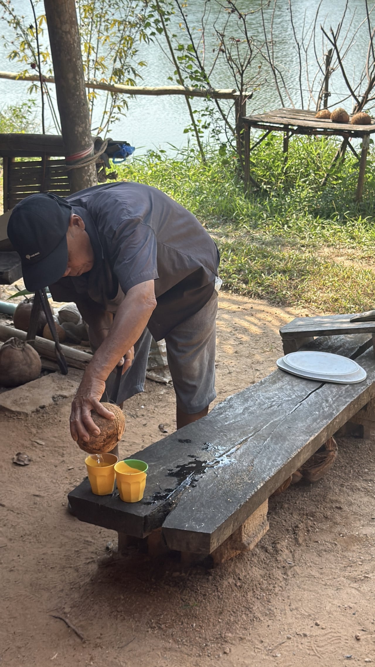 Muž v přístřešku u řeky lije kokosovou vodu do kelímků